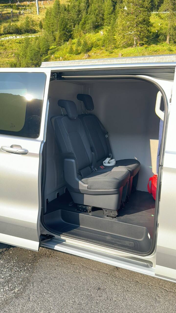 Viewed from the side, an E-Transit van door is open, showing two seats inside.